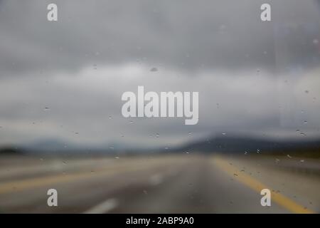 La pioggia caduta sul vetro dell'auto strada con nebbia o foschia nella natura verde . Gocce d'acqua sul vetro in auto . gocce di pioggia Foto Stock