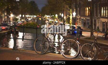 Un night shot di una bicicletta incatenato ad un ponte su un canale ad Amsterdam nei Paesi Bassi Foto Stock