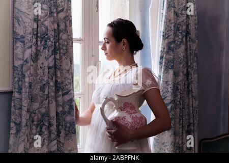 Giovane donna in autentici regency abito vicino a una finestra di un classico interno Foto Stock