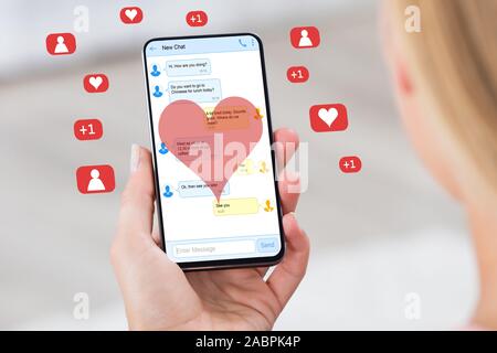 Donna chat di lettura sul telefono cellulare circondato da icone e forme di cuore Foto Stock