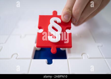 Una persona che collega ultimo pezzo rosso con simbolo di paragrafo nel puzzle rompicapo Foto Stock