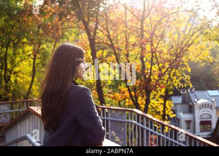 Un giovane caucasico bella ragazza con i capelli scuri passeggiate in giro per la città e guarda il luminoso autunno gli alberi del parco. Foto Stock