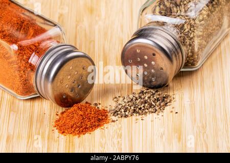 Gli shaker pieno di pepe nero macinato e paprika rossa su uno sfondo di legno Foto Stock