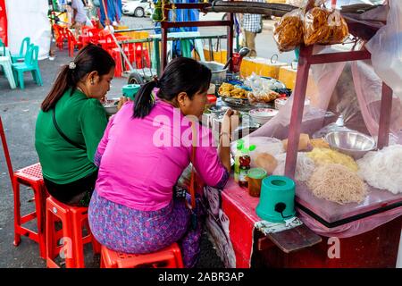 Due donne mangiare cibo di strada da uno stallo nel centro di Yangon, Yangon, Myanmar. Foto Stock