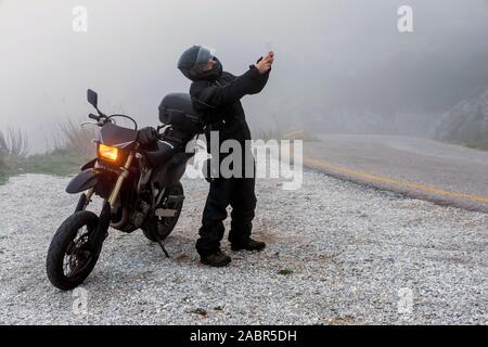 Rider è il tentativo di trovare il segnale sul suo cellulare su un nebbioso giorno ride su per le montagne con la sua moto - avventura progetto ride Foto Stock