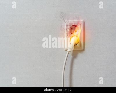 Corto circuito elettrico a causa incendio sulla presa di corrente. Le fiamme e il fumo sul filo elettrico plug. Foto Stock