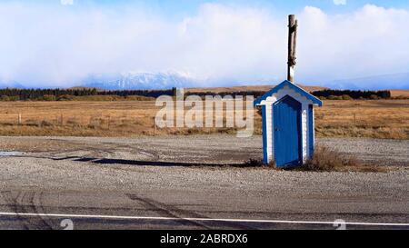 Una vecchia casella con una porta blu in piedi sul lato della strada in Nuova Zelanda con uno sfondo di coperta di neve montagne alpine Foto Stock