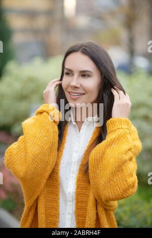 Bella acconciatura. Nizza dai capelli scuri donna sorridente mentre che fissa i suoi capelli Foto Stock