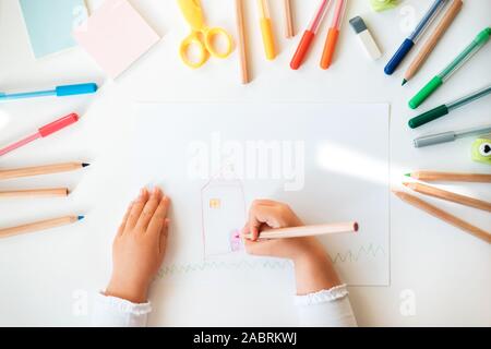 Chiusura del bambino con le mani in mano disegno nel libro bianco all'interno colorato Matite e penne. Foto Stock