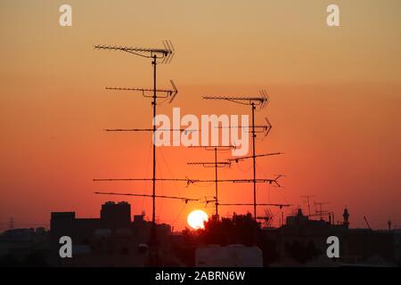 Antenne televisive e parabole satellitari stagliano contro una regolazione del sole Foto Stock