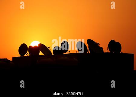 Antenne televisive e parabole satellitari stagliano contro una regolazione del sole Foto Stock