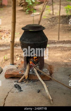 Gli abitanti di un villaggio di bollito di acqua calda dalla stufa. Il riscaldamento di una pentola grande di acqua in India rurale Foto Stock