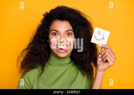 Close up foto di allegro carino carina ragazza positiva toothily sorridente con la lingua fuori tenendo la carta con il suo isolato emoji colori vividi Foto Stock