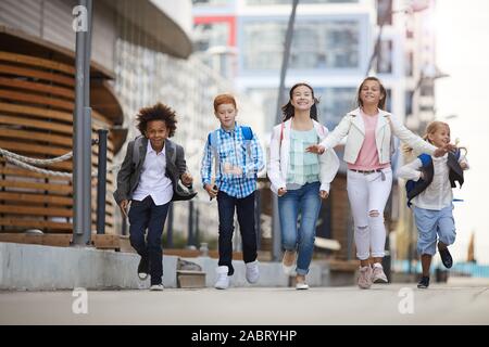 Gruppo di scuola multietnica i bambini in esecuzione insieme lungo la strada dopo la scuola Foto Stock