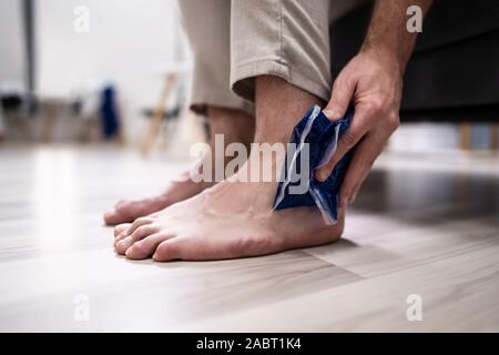 Close-up di persona della mano che tiene il gel del ghiaccio Pack su caviglia a casa Foto Stock