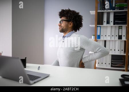 Giovane imprenditore con Backpain seduti su una sedia al lavoro Foto Stock