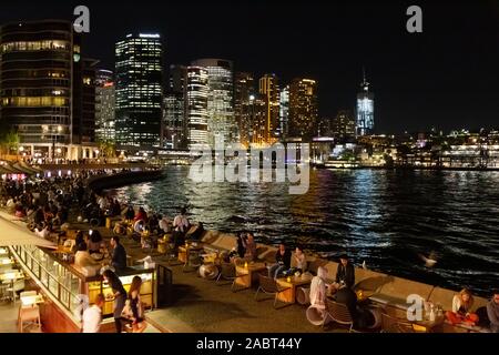 Notte di Sydney e il Sydney Harbour e Circular Quay di notte, con grattacieli e persone di mangiare al Bar Opera in primavera; Sydney Australia Foto Stock