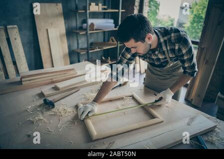 Foto di focalizzato l'uomo gravi concentrata sulla misura della lunghezza del telaio in legno correttamente utilizzando la linea del nastro Foto Stock