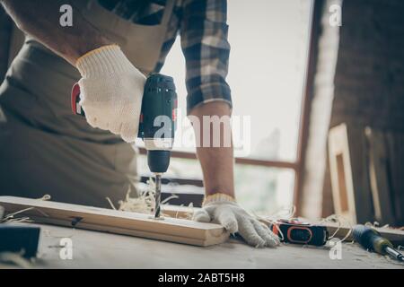 Ritagliato clsoe fino foto di un uomo per forare il legno in dotazione con i guanti facendo il suo lavoro indoor utilizzando moderni strumenti Foto Stock