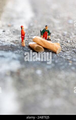 Due minuscoli immondizia puliscono e spazzano le sigarette fumate sulla strada che inquinano l'ambiente Foto Stock