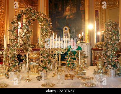 Un Royal Collection Trust membro del personale mette i tocchi di rifinitura per il gran servizio nello Stato sala da pranzo al Castello di Windsor, Berkshire. Foto Stock