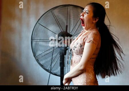 Stanco ed annoiato imbardata donna nella parte anteriore del ventilatore gigante. Hanoi. Il Vietnam. Foto Stock