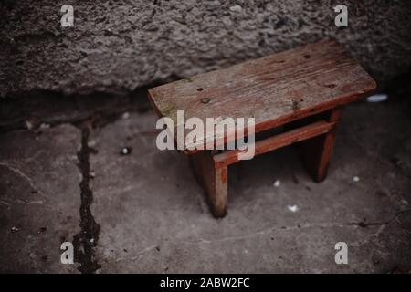 Piccola vecchia sedia in legno in un cortile rurale dalla parete. Foto Stock