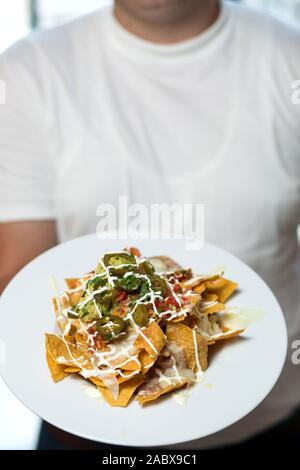 Chi detiene un piatto di nachos con tortilla chips Foto Stock