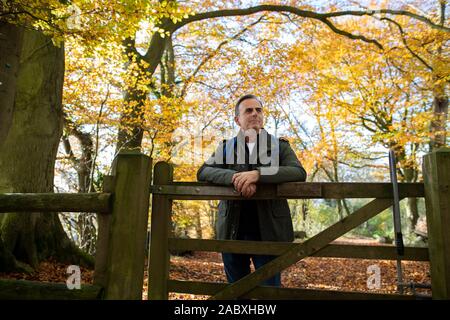 Active uomo maturo appoggiata sul cancello di legno a piedi attraverso il bosco in autunno Foto Stock