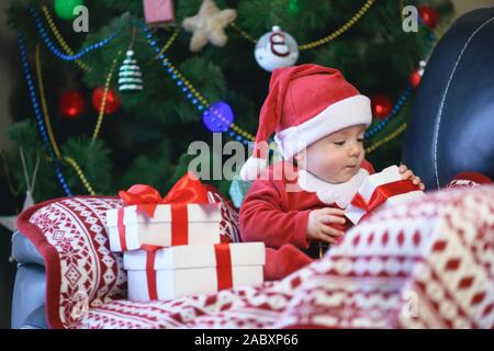 Baby boy in abiti da Babbo Natale Natale tenendo presente confezione regalo nella parte anteriore dell albero di Natale Foto Stock