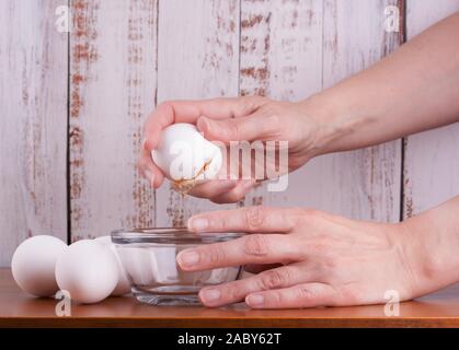 Mano femmina broking un bianco uova crude come ingrediente pronto per cucinare Foto Stock