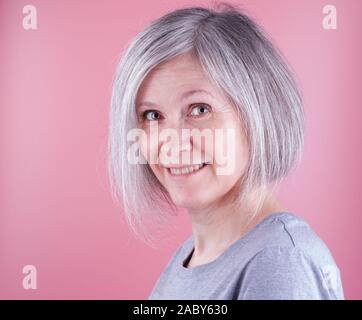Close-up ritratto di una donna nei primi anni cinquanta con i capelli grigi, sfondo rosa Foto Stock
