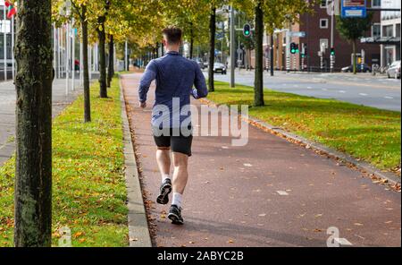 Jogging nel centro della citta'. Rotterdam Paesi Bassi. Vista posteriore di un forte uomo correre tutto solo su un asfalto rosso pista ciclabile. Uno stile di vita sano Foto Stock