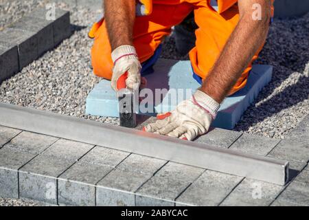 Builder mani guantate la posa di pavimentazioni per esterni di mattoni su una base preparata. Foto Stock