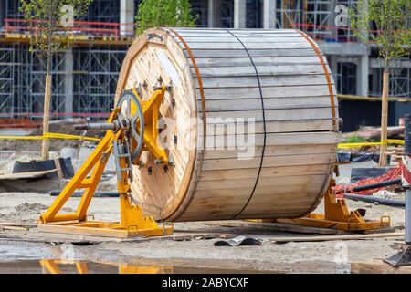Sito in costruzione con grande tamburo per cavi. Bobina in legno del cavo esterno. Grande bobina in legno. Rocchetto con cavo. Foto Stock
