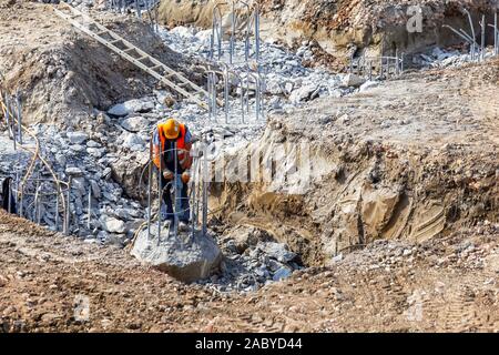 Operaio edile utilizzando jackhammer e rompendo il calcestruzzo rinforzato pile al sito in costruzione. Foto Stock