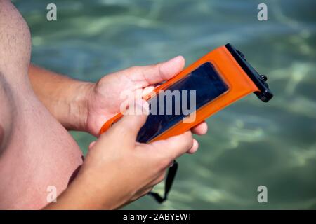 L'uomo detiene una custodia impermeabile per il telefono in mano, stando in mare. PVC chiusura a zip in sacchetto di proteggere il telefono cellulare da acqua. Foto Stock