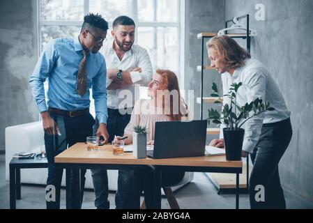 Discutere i metodi. Young business team che lavora su un progetto con il computer portatile sul tavolo e sorridente Foto Stock