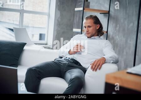 Vista frontale. Giovane uomo seduto in una parte anteriore del notebook e di bere whisky Foto Stock