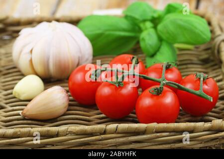 Selezione di freschi ingredienti organici per la pasta: pomodori ciliegia, aglio e basilico sul vassoio di vimini Foto Stock