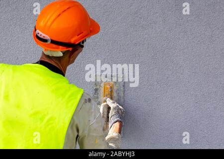 Lavoratore applicando intonaco decorativo sulla parete per mezzo di una spatola di acciaio. Il cemento bianco in base decorativo rivestimento superiore del gesso resistente all'esterno se le condizioni. Foto Stock