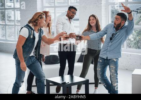 Andiamo a fare un colpo. I giovani aventi un buon tempo in ufficio. Sorridente e bere con windows a sfondo Foto Stock