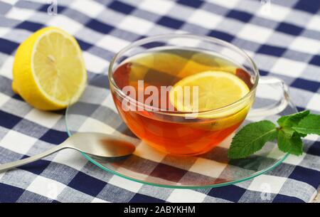 Tè al limone in coppa trasparente sul panno a scacchi Foto Stock