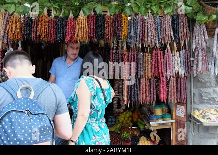 TBILISI, GEORGIA - Giugno 7, 2019: una ragazza compra un churchkhela da un uomo. Ampia selezione di dolci georgiano sul mercato a Tbilisi. Turisti scelgono de Foto Stock