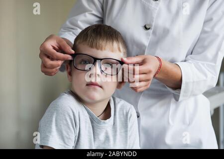 Ti stai chiedendo il bambino. Ragazzo seduto in ufficio medico e cercando nuovi occhiali blu Foto Stock
