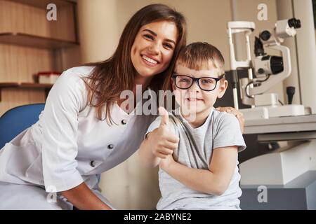 Occhio femminile medico seduta con il bambino dopo aver eseguito la prova di visione Foto Stock