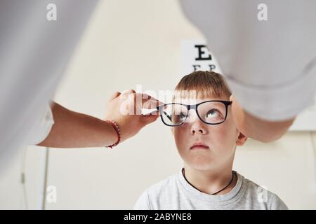 Ragazzo che guarda a specifiche. Medico dare al bambino nuovi occhiali neri per la sua visione Foto Stock