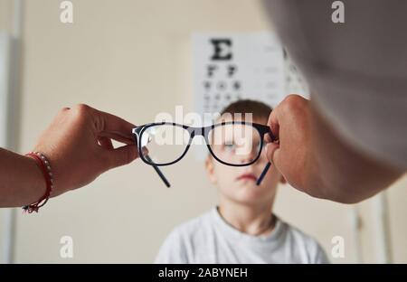 Messa a fuoco su specifiche. Medico dare al bambino nuovi occhiali neri per la sua visione Foto Stock