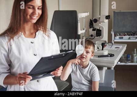 Donna sorridente durante il processo. Facendo il test nell'oculista di office con un bambino. Medico note i dati