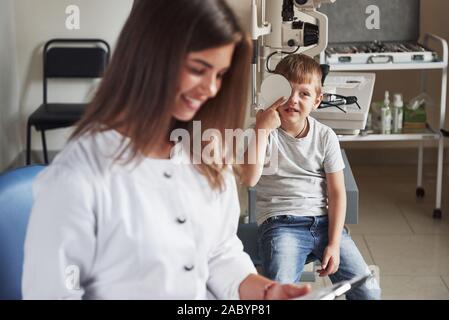 Copertura di occhio destro. Facendo il test nell'oculista di office con un bambino. Medico note i dati Foto Stock